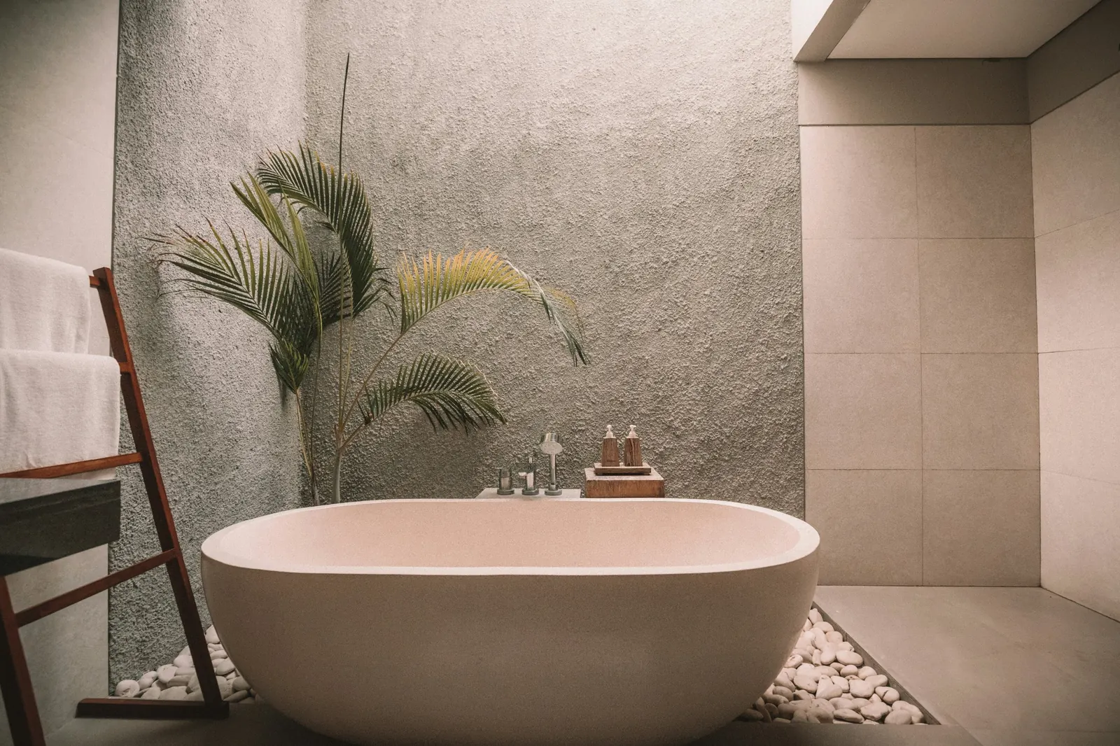 Freestanding stone bathtub beside a decorative palm and pebbles in a bathroom