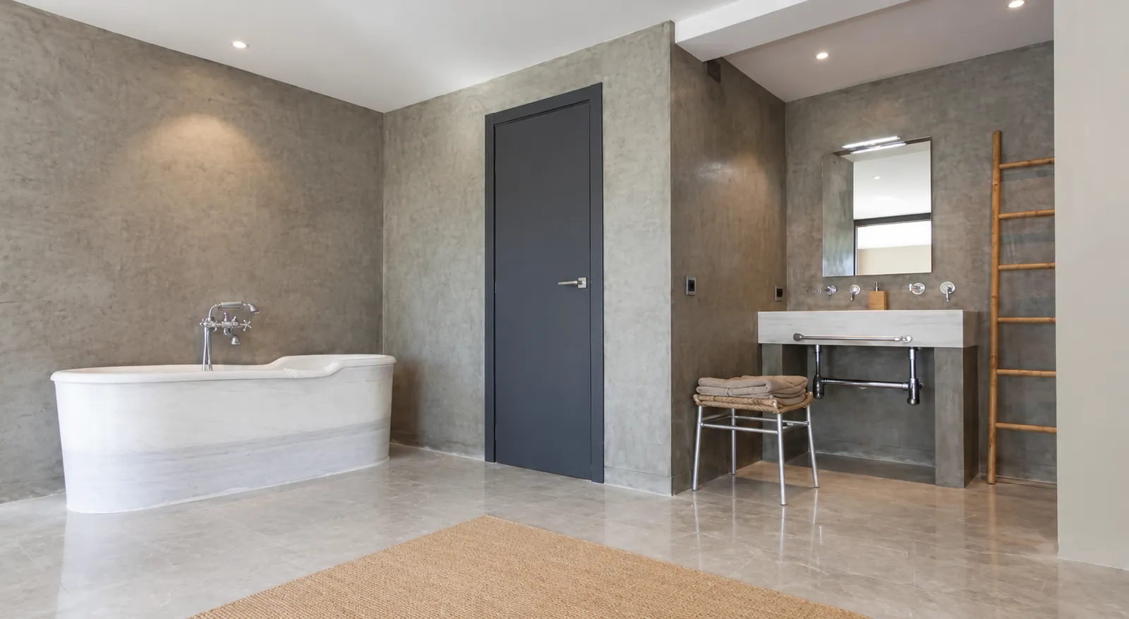 Spacious bathroom with seamless wall finish, freestanding marble bath and wall-hung washbasin